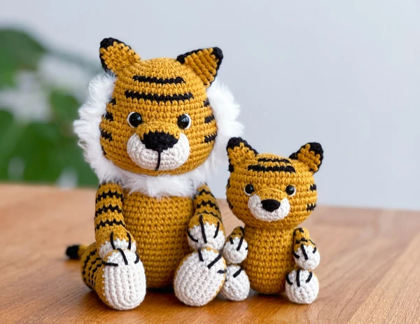 Crochet mother tiger toy and crochet baby tiger toy sitting next to each other.