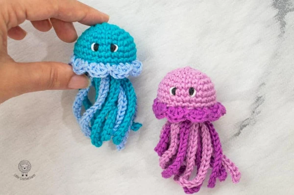 A bright blue and a bright pink pair of crochet jellyfish toys.