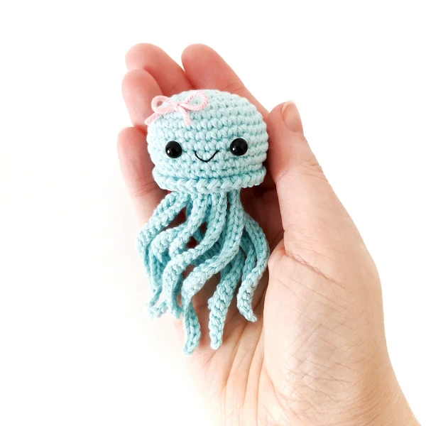 A pale blue mini jellyfish amigurumi with a pink bow,