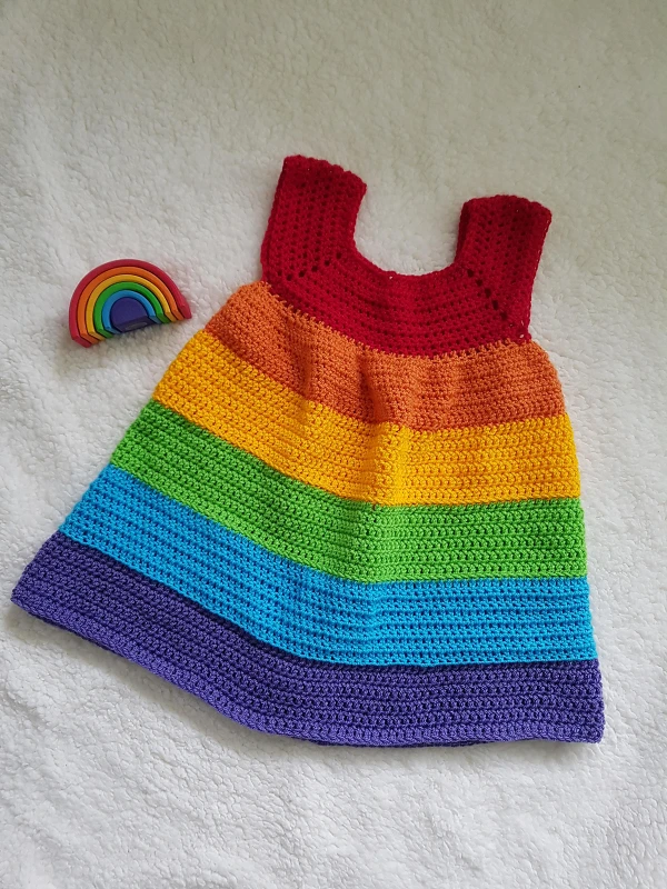 A children's crochet dress with rainbow coloured stripes.