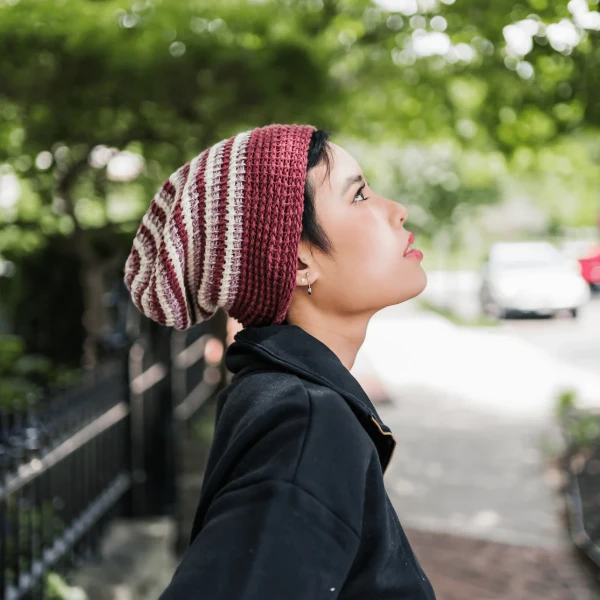 A woman in a park wearing a striped Tunisian crochet hat.