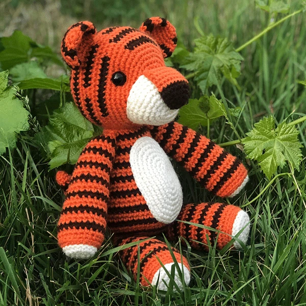 A crocheted stuffed toy tiger sitting in the grass.