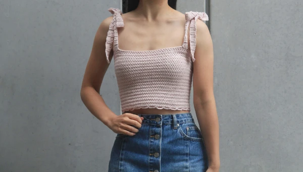 A woman wearing a cropped crochet tank top with tie straps.