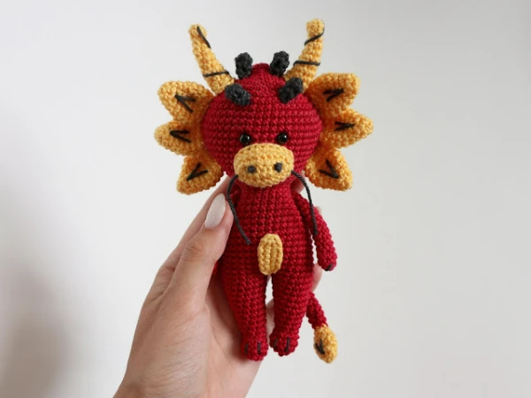 A small red and yellow crochet dragon amigurumi.