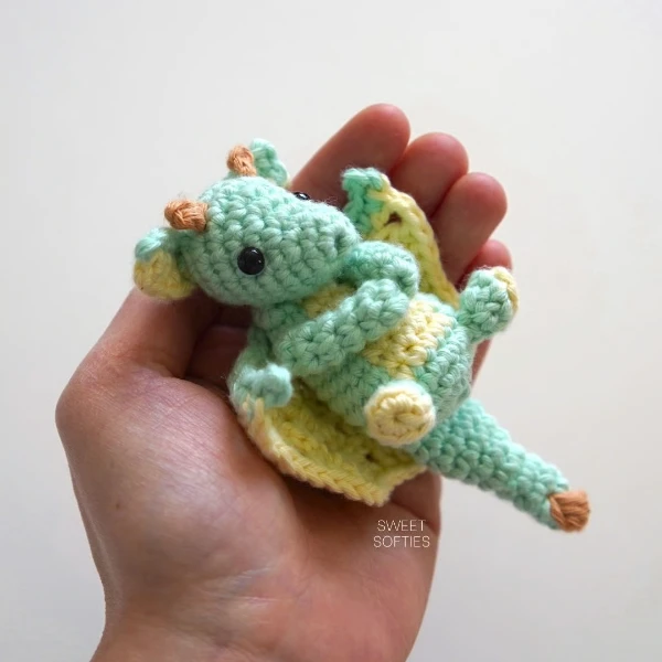 A miniature crochet dragon in the palm of a hand.
