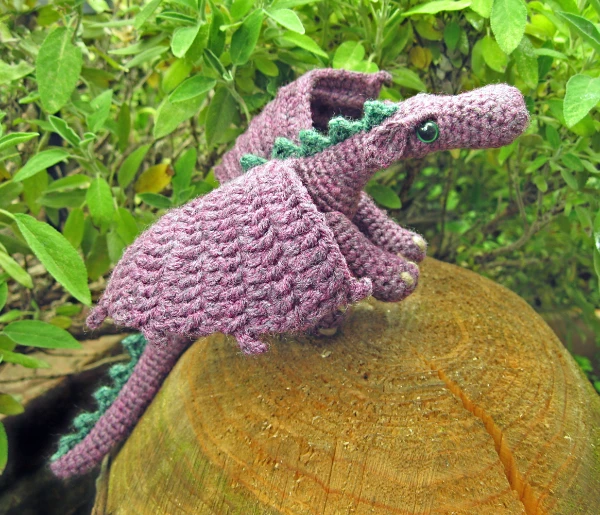 A purple and green crochet dragon toy.