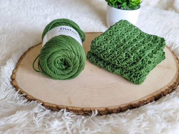 A green suzette stitch crochet dishcloth next to a ball of yarn.