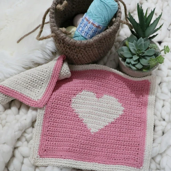 A pink dishcloth with a tapestry crochet heart motif.