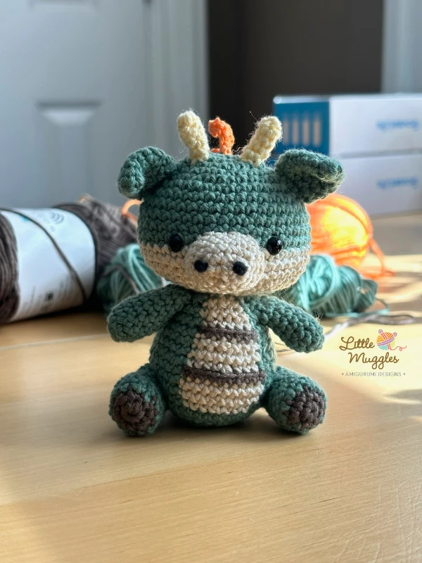 A seated mini crochet dragon toy.