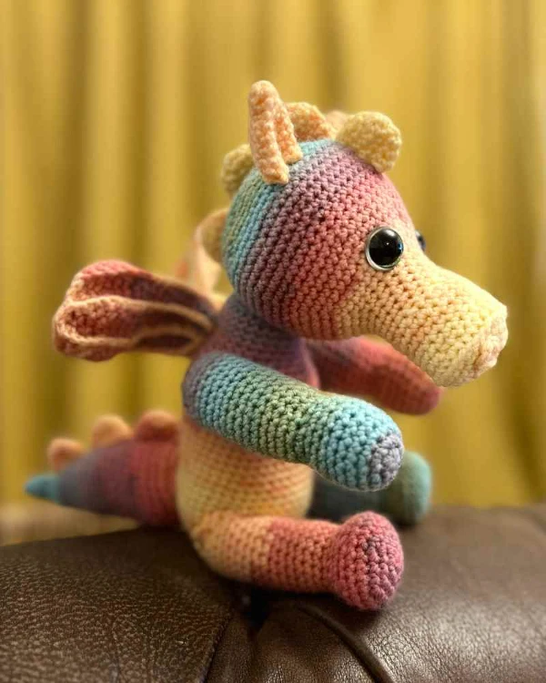 A cute crochet dragon toy made with rainbow variegated yarn.