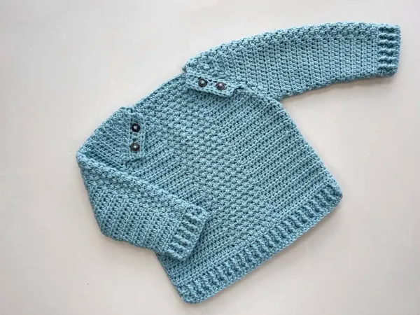 A crocheted baby sweater with buttons on shoulders.