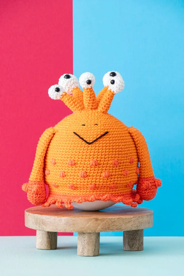 An orange crochet monster with multiple tentacle eyes.