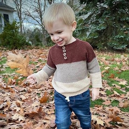 A young boy wearing a brown striped crochet sweater.