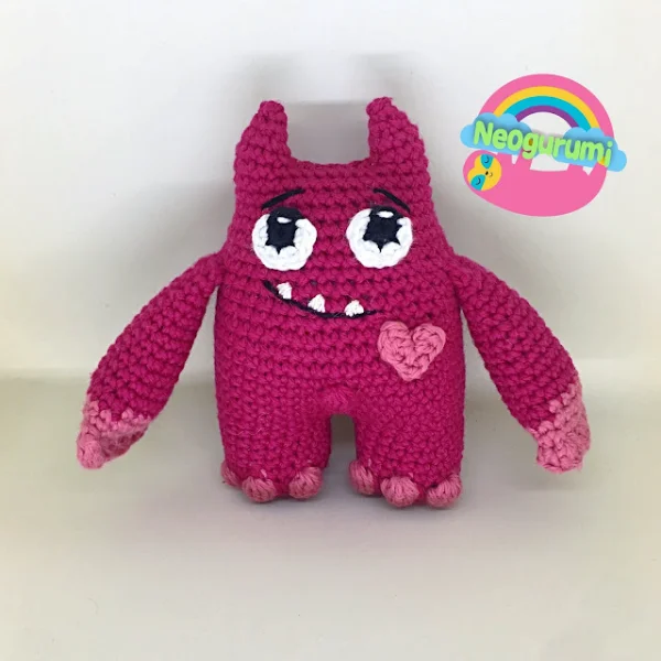 A pink crochet love monster with horns and a goofy grin.