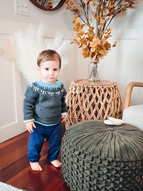 A toddler wearing a crochet sweater with mosaic details.