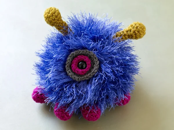 A fluffy blue one-eyed monster crochet toy.