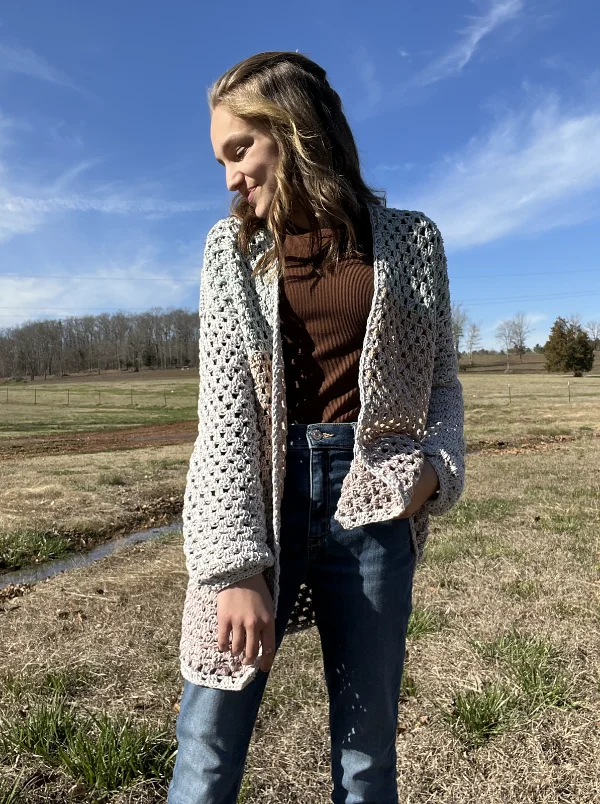 A woman wearing a crochet granny stitch cardigan with jeans.