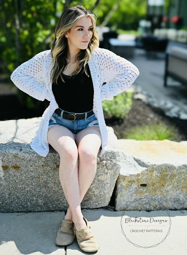 A woman wearing a white, oversized granny stitch cardigan.