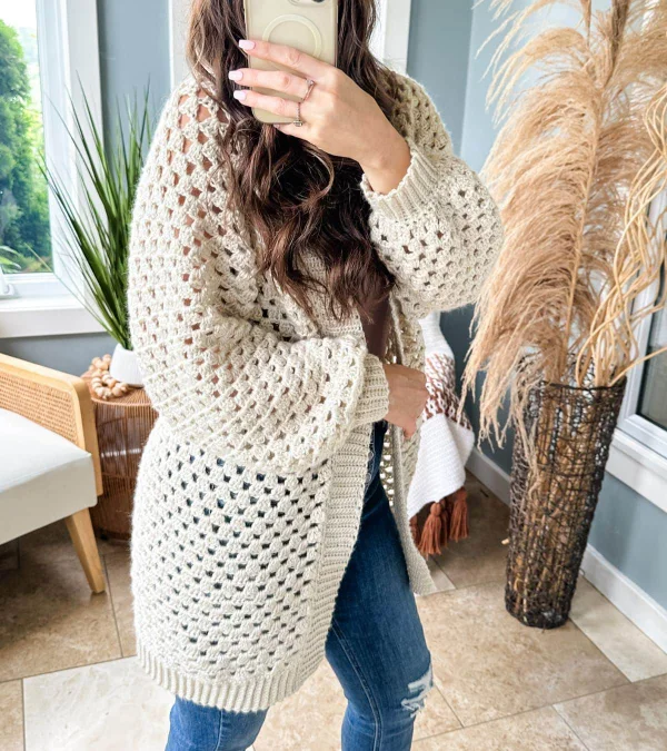 A woman wearing a long, cream-coloured granny stitch crochet cardigan.