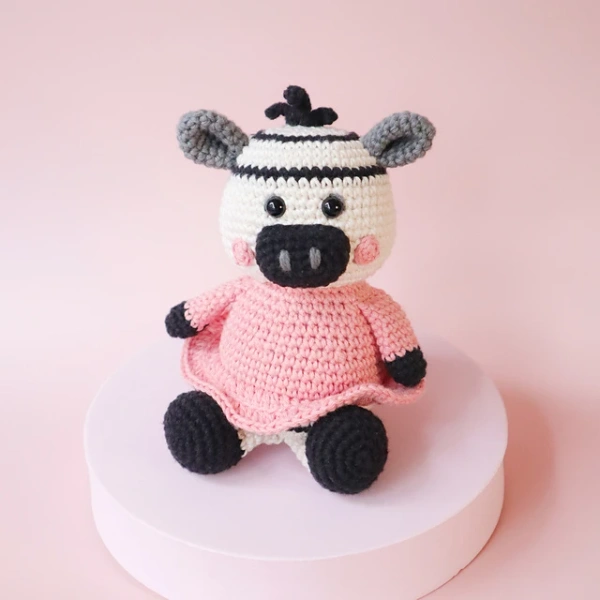A crochet zebra toy wearing a pink dress.
